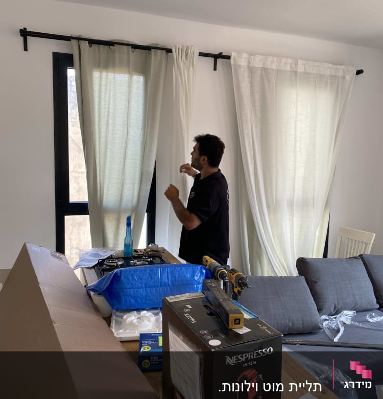 אדם מתקין וילון עם מקדחה על חלון